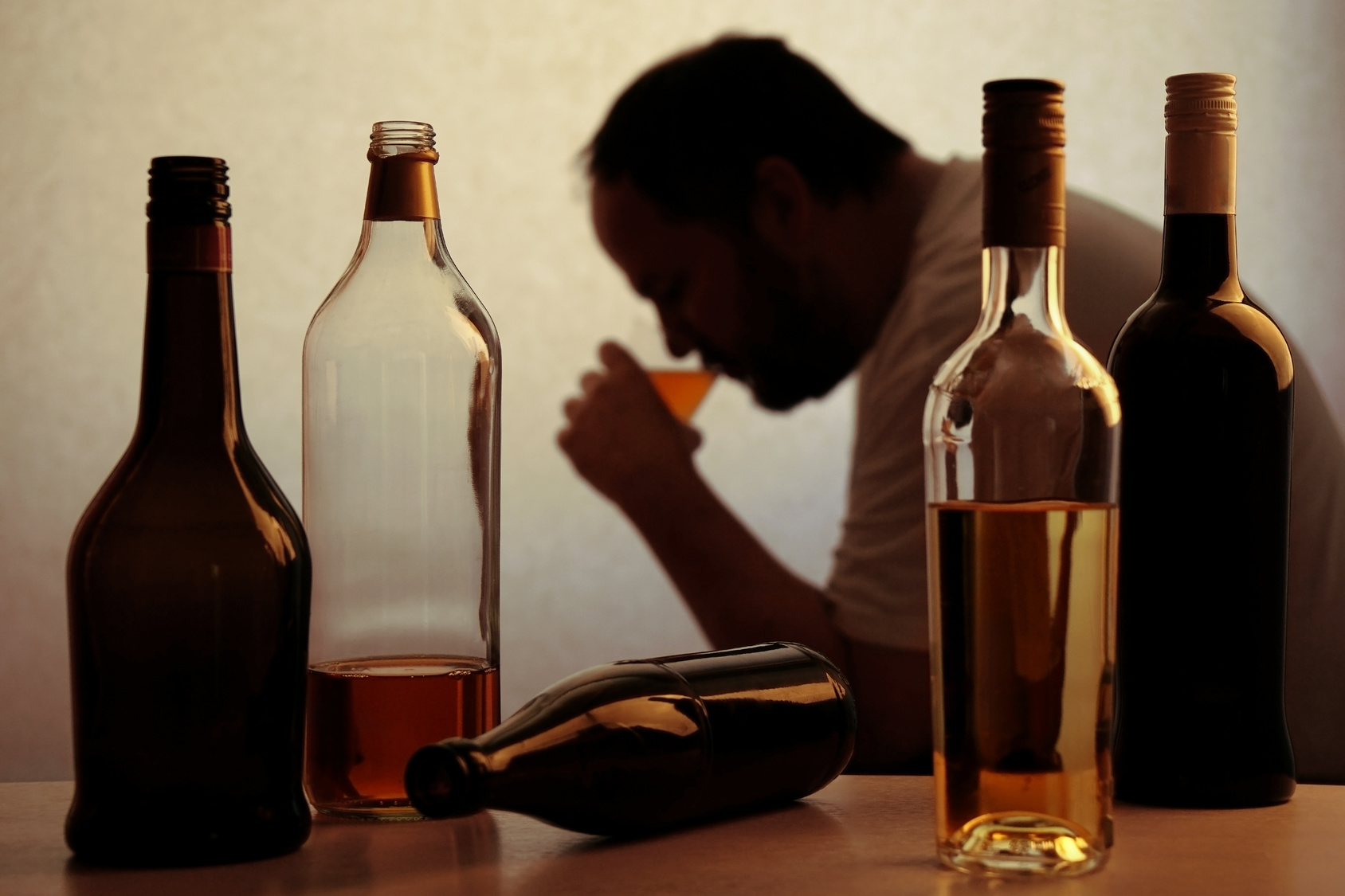 silhouette of anonymous alcoholic person drinking behind bottles of alcohol